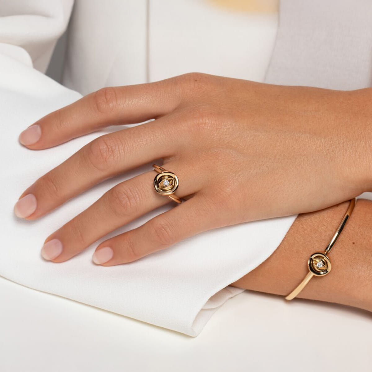 Eine Hand mit sauber manikürten Nägeln ruht auf einer weißen Fläche, geschmückt mit einem Jörg Heinz Ringe Goldring mit rundem Edelstein und einem passenden Goldarmband mit ähnlichem Edelsteinbesatz.