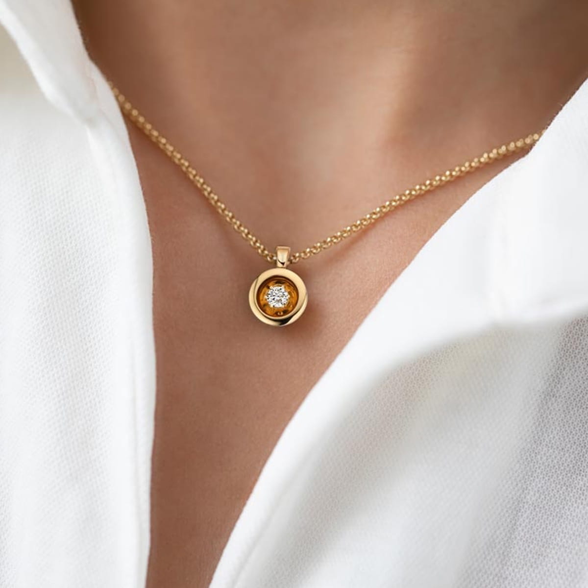 Nahaufnahme einer Person, die eine goldene Jörg Heinz-Halskette mit einem runden Anhänger mit einem funkelnden Edelstein in der Mitte trägt, kombiniert mit einem weißen Hemd mit Kragen.