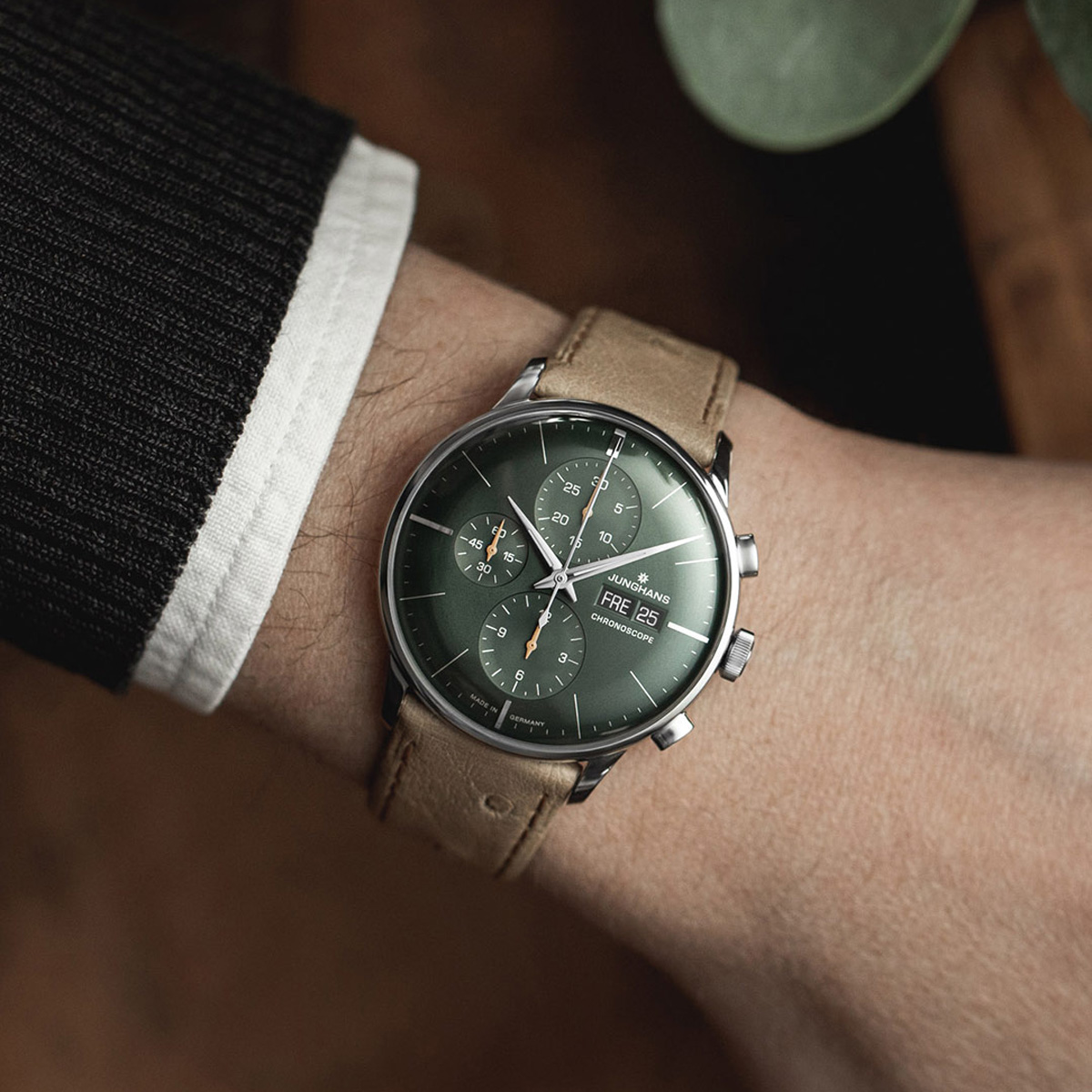 JUNGHANS © 2026 Eine Person trägt eine Junghans Meister Automatik Armbanduhr mit grünem Zifferblatt, mehreren Hilfszifferblättern und einem hellbraunen Lederarmband. Die Uhr befindet sich am linken Handgelenk, gepaart mit einem dunklen Pullover und einer weißen Manschette.