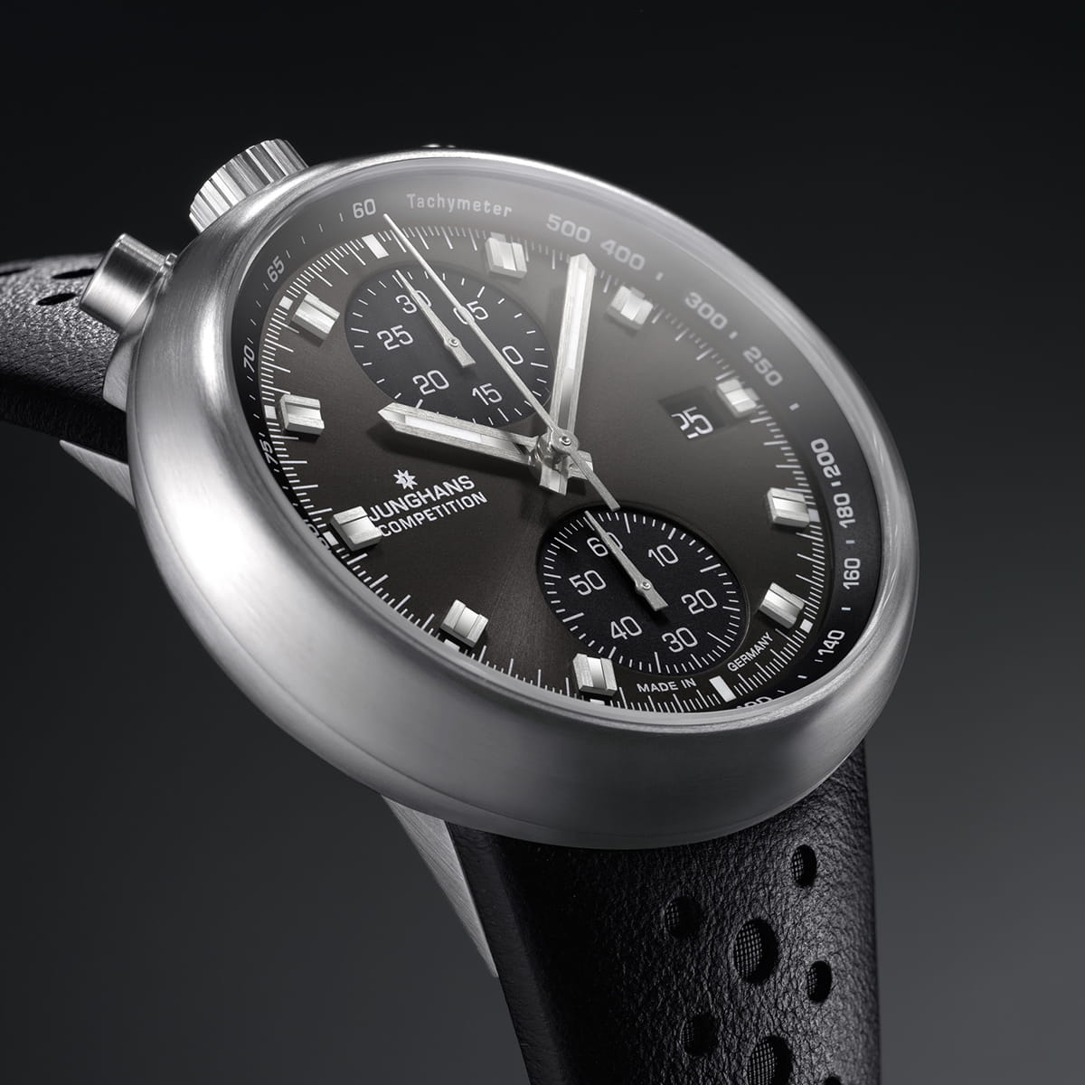 Nahaufnahme einer modernen Junghans Sport-Chronographen-Armbanduhr mit schwarzem Zifferblatt, silbernen Akzenten und drei Hilfszifferblättern, einer Tachymeterskala und einem schwarzen perforierten Lederarmband vor dunklem Hintergrund.