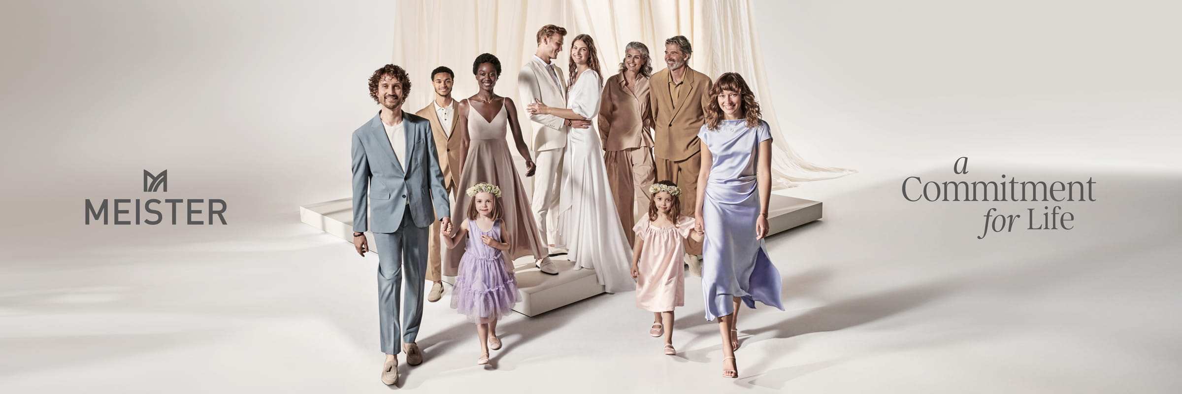 MEISTER © 2026 Eine bunt gemischte Gruppe von Erwachsenen und Kindern in eleganter pastellfarbener Kleidung schreitet lächelnd unter einem drapierten weißen Stoff voran. Der Text lautet "MEISTER" und spiegelt Meisters Engagement für das Leben wider.