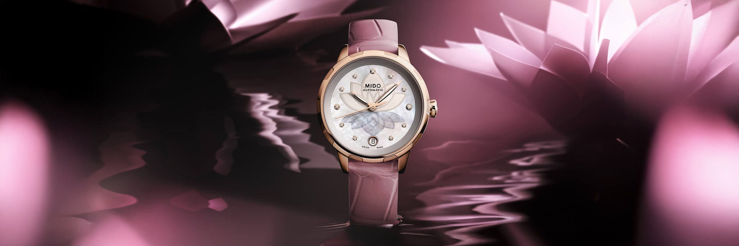Die roségoldene Armbanduhr Mido Rainflower mit Perlmuttzifferblatt präsentiert sich vor einem verträumten, rosafarbenen Hintergrund mit Wasserreflexen und abstrakten, leuchtenden Lotusblumen.