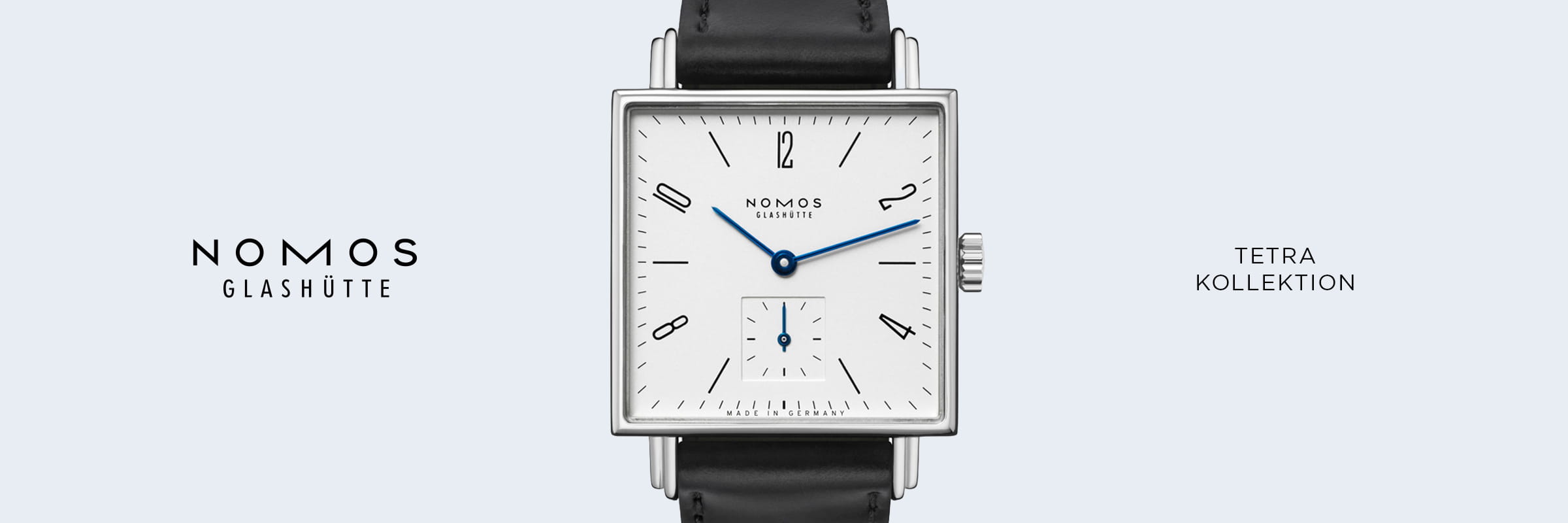 Eine quadratische NOMOS-Tetra-Armbanduhr mit weißem Zifferblatt, schwarzen Indizes, blauen Zeigern und schwarzem Lederarmband steht mittig auf hellgrauem Grund, eingerahmt vom Schriftzug "NOMOS GLASHÜTTE TETRA KOLLEKTION" auf beiden Seiten.