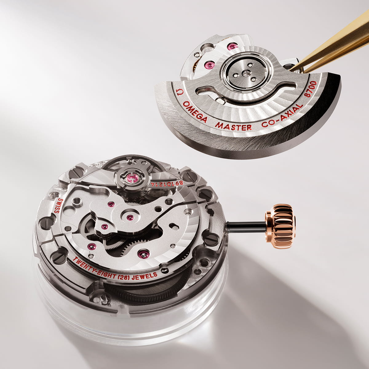 OMEGA © 2026 Nahaufnahme eines OMEGA Master Co-Axial Uhrwerks bei der Montage; eine Hand hält einen Rotor über dem komplizierten Mechanismus, der Zahnräder, Edelsteine und eine Krone aus Roségold zeigt.