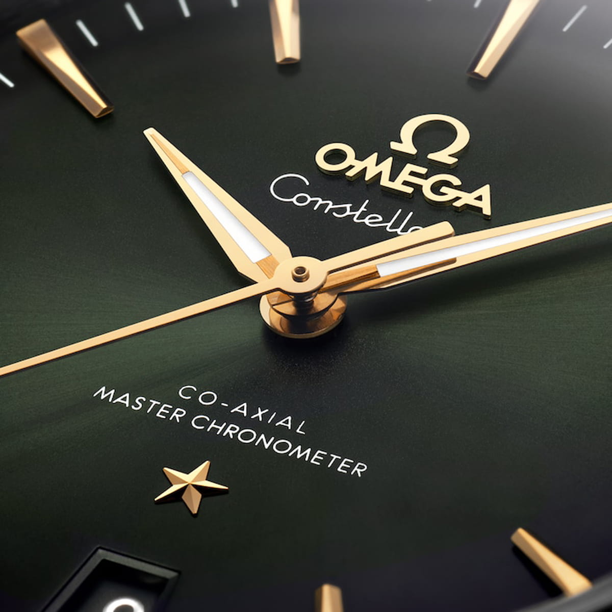 Nahaufnahme eines grünen Zifferblatts der OMEGA Constellation mit goldenen Zeigern, goldenen Indexen, einem goldenen Stern und den Worten "Co-Axial Master Chronometer" und "OMEGA Constellation" in eleganter weißer und goldener Schrift.
