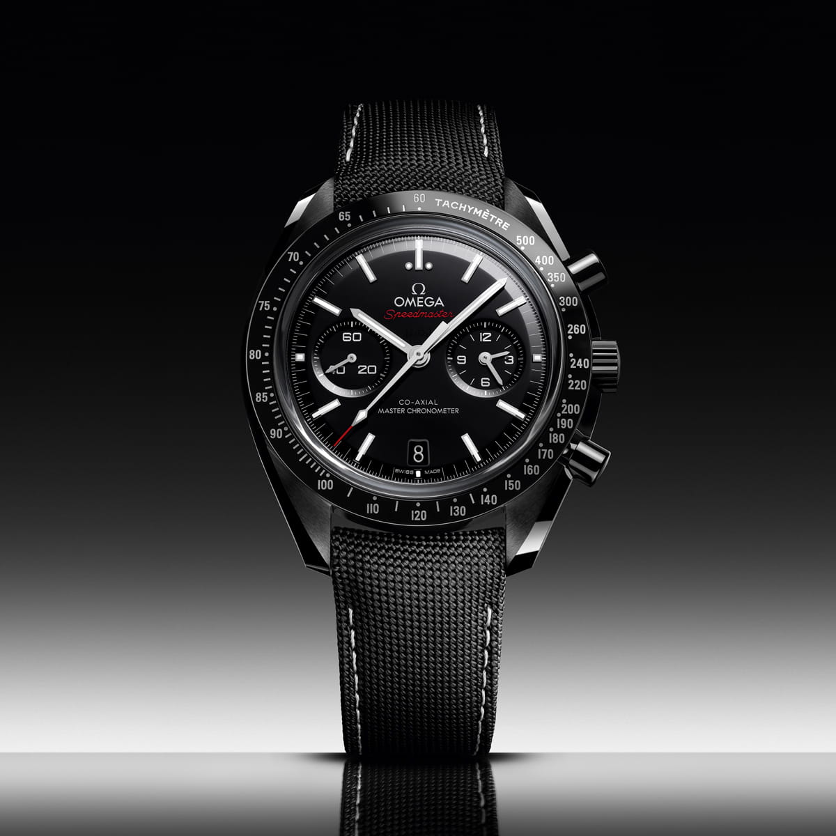Eine schwarze OMEGA Dark Side of the Moon Speedmaster Uhr mit strukturiertem Armband, schwarzem Zifferblatt, weißen Indexen, Hilfszifferblättern und Tachymeterlünette vor einem Hintergrund mit Schwarz-Weiß-Verlauf.