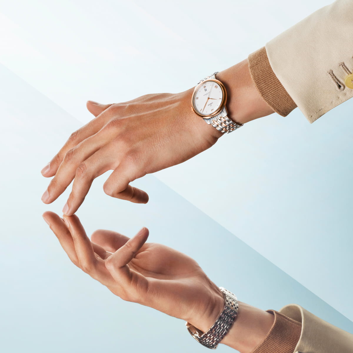 OMEGA © 2026 Eine Hand, die eine silberne OMEGA Prestige Armbanduhr mit weißem Ziffernblatt trägt, spiegelt sich unten auf einer glatten Oberfläche vor einem hellblauen Hintergrund. Das Handgelenk ist mit einer beigen Jacke mit brauner Manschette bekleidet.