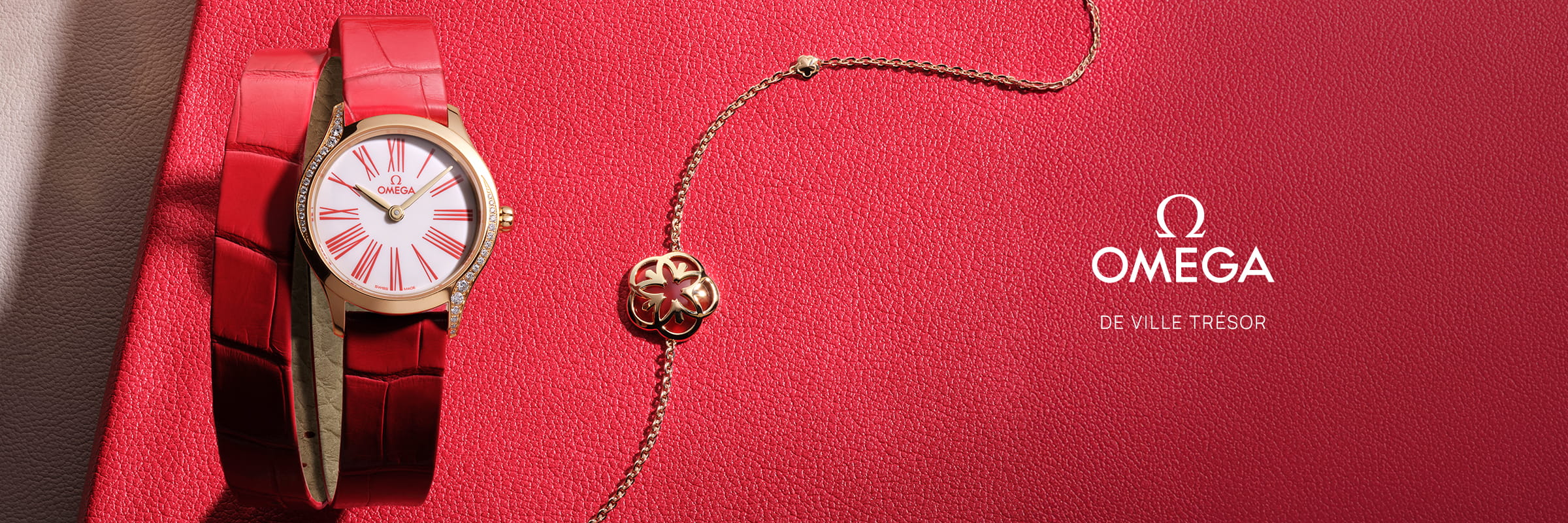 OMEGA © 2026 Eine goldene OMEGA Trésor De Ville Uhr mit rotem Lederarmband und passender goldener Kleeblatt-Halskette, die elegant auf einer strukturierten roten Oberfläche neben dem Omega-Logo und dem Text "DE VILLE TRÉSOR" präsentiert wird.