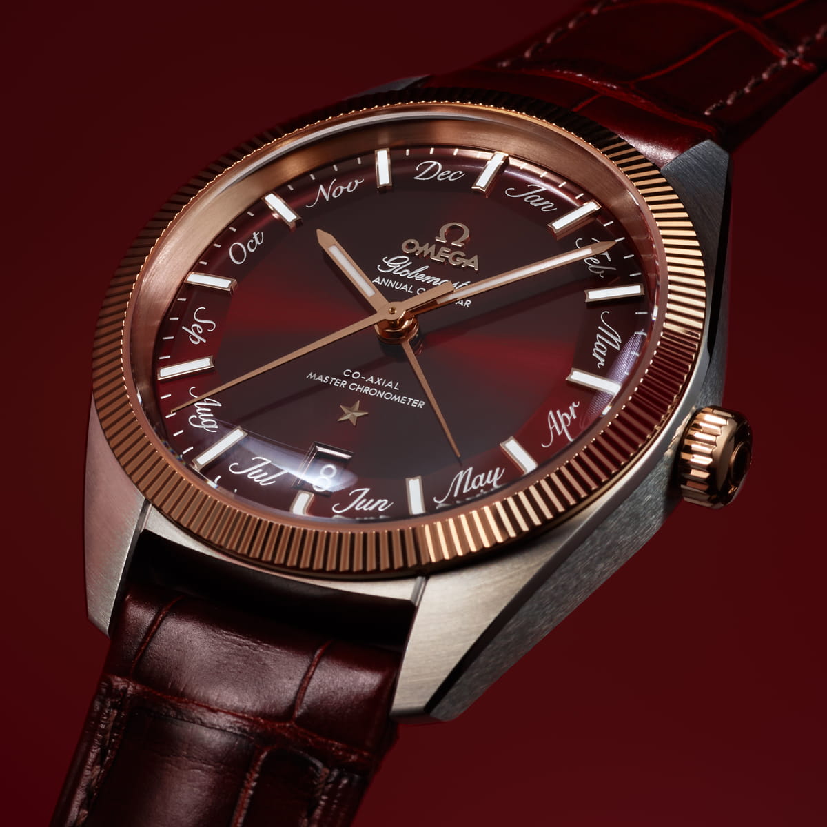 OMEGA © 2026 Eine luxuriöse OMEGA Globemaster Armbanduhr mit rotbraunem Zifferblatt, goldenen Akzenten und einem braunen Lederarmband. Auf dem Zifferblatt sind die Monatsnamen in eleganter Schrift am äußeren Rand vor einem tiefroten Hintergrund mit Farbverlauf zu sehen.