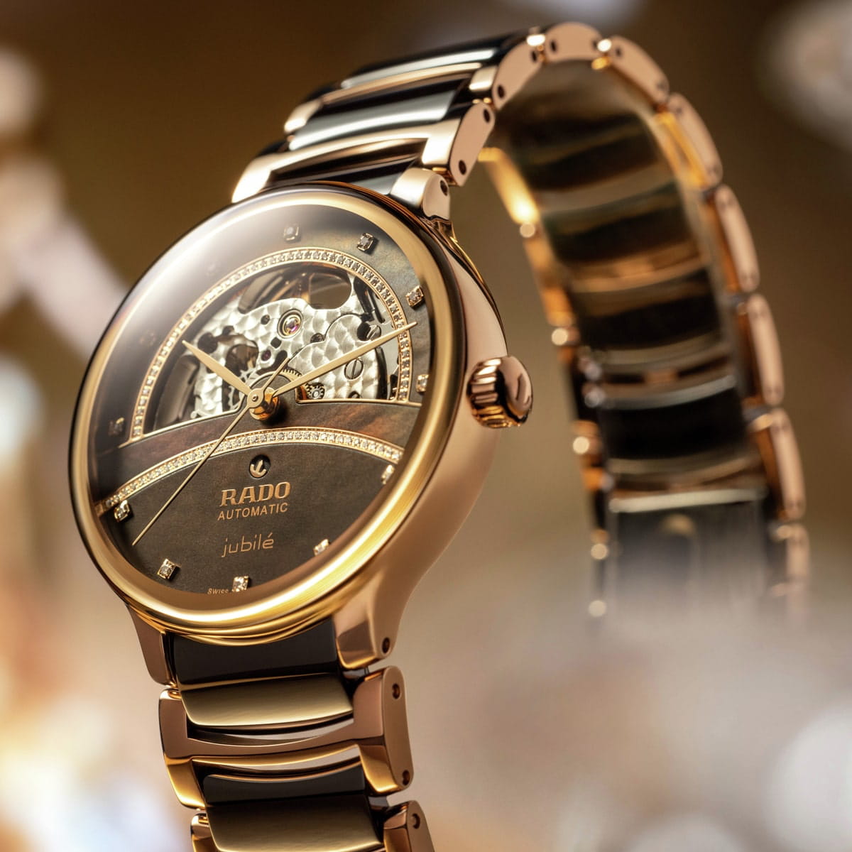 Eine luxuriöse Rado Centrix Automatik-Armbanduhr mit roségoldenem Metallband und Lünette, einem teilweise offenen skelettierten Zifferblatt, diamantenen Akzenten und der Aufschrift "jubile" auf dem Zifferblatt, das in einer sanft beleuchteten Umgebung präsentiert wird.