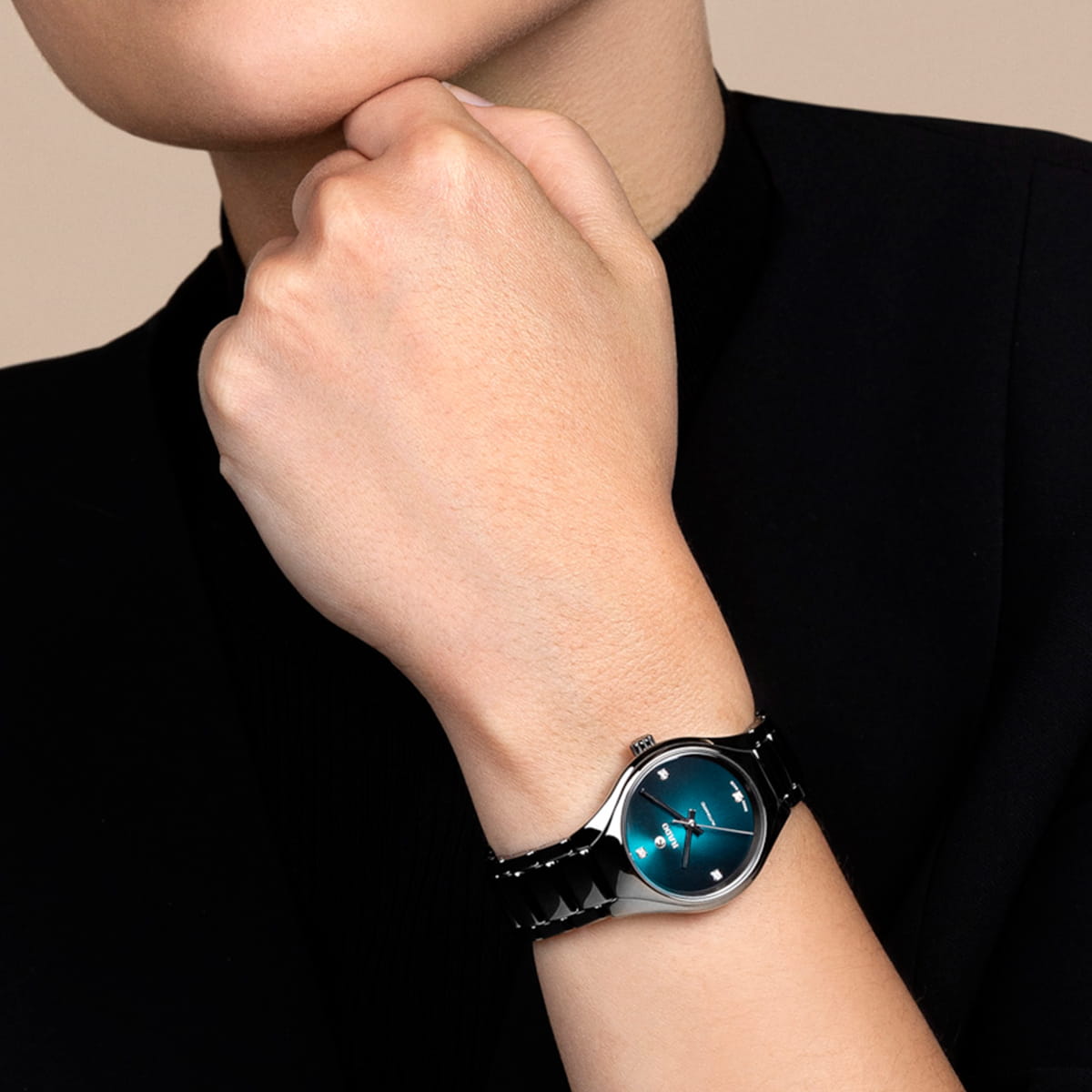Eine schwarz gekleidete Person hält ihre Hand an ihr Gesicht und präsentiert eine Rado True Round Armbanduhr mit einem blaugrünen Zifferblatt und einem schwarzen Metallband.