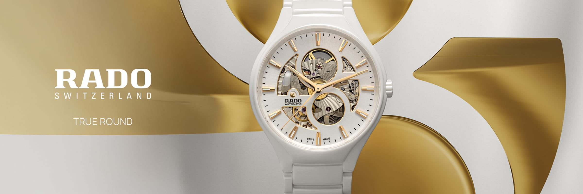 Eine weiße Rado True Round Switzerland Skelettuhr mit goldenen Akzenten wird durch abstrakte goldene und silberne Formen in Szene gesetzt. Das teilweise transparente Zifferblatt gibt den Blick auf die komplizierte innere Mechanik frei.